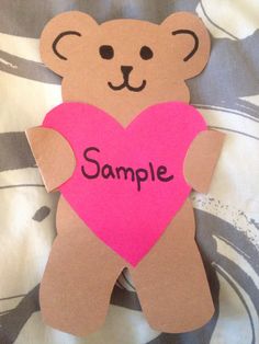 a brown teddy bear holding a pink heart with the word sample written on it's chest