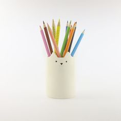 a white cup with colored pencils in it and a cat face on the side