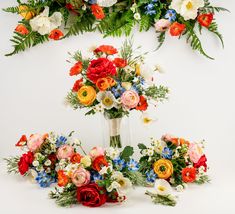 an arrangement of colorful flowers in a vase on a white background with greenery around it