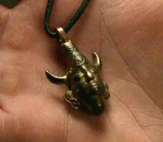 a hand holding a small brass necklace with an animal on it