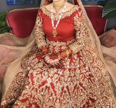 a woman in a red and gold bridal gown sitting on a couch with her hands behind her head