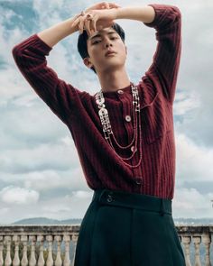 a young man in a red sweater and black pants poses with his hands on his head