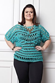 a woman standing in front of a white wall wearing black pants and a turquoise crochet top