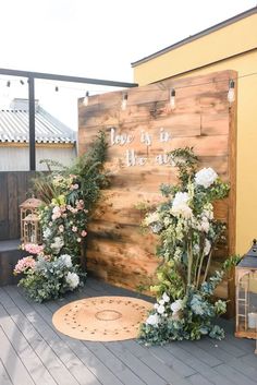 an outdoor area with flowers and greenery on the ground next to a wooden wall