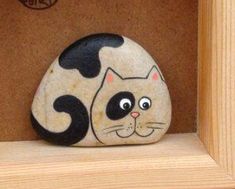 a rock with a cat painted on it sitting in a wooden box next to a sign