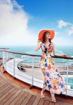 a woman in a long dress and orange hat standing on the deck of a cruise ship