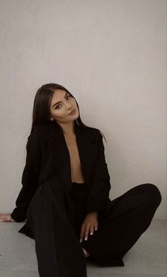 a woman is sitting on the floor in black pants and a blazer with one hand on her hip