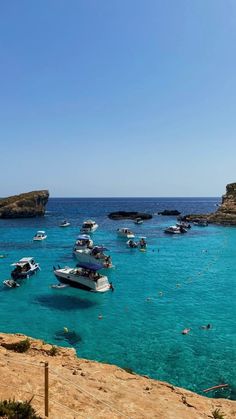 several boats floating in the blue water near some rocks and cliffs on a sunny day