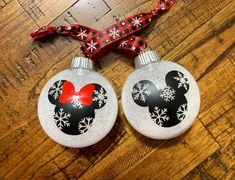 two mickey mouse christmas ornament ornaments on a wooden floor with a red ribbon