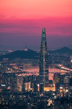 the city skyline is lit up in pink and blue at night, as seen from an observation point