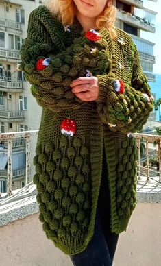 a woman standing in front of a tall building wearing a green knitted cardigan