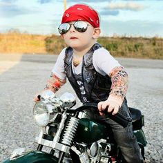 a little boy sitting on top of a motorcycle wearing sunglasses and a red bandana