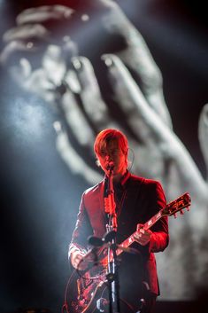 a man with an electric guitar on stage in front of a large hand projected behind him