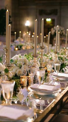 a long table with white flowers and candles on it is set for a formal dinner