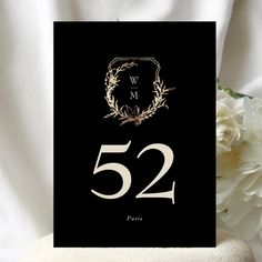 a black and gold wedding table number card with white flowers in the background on a chair