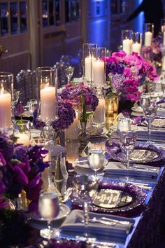 the table is set with purple and white flowers, silverware, candles and plates