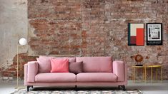 a pink couch sitting in front of a brick wall next to a table with a lamp on it