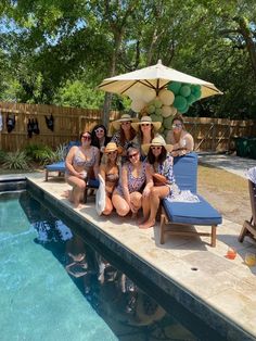 a group of women sitting next to a pool under an umbrella