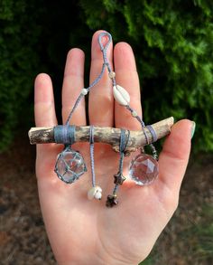 a hand holding a piece of wood and some beads on it's end with a tree branch in the background