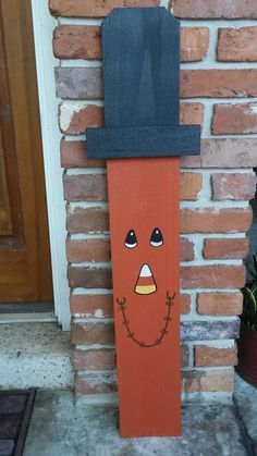 a wooden sign with a face painted on it's side by a brick wall