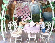 two children sitting at a table in front of a gazebo with flowers on it