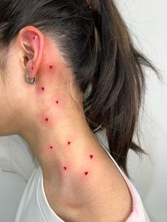 a woman's back neck with small red hearts on her left side behind the ear