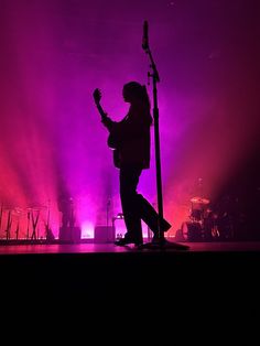 a man standing on top of a stage with a guitar in his hand and purple lighting behind him