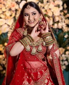 a woman in a red and gold bridal outfit posing for the camera with flowers behind her