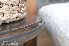 a basket sitting on top of a wooden table next to a white bedding sheet