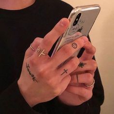 a person holding a cell phone with tattoos on their fingers and wrist, while wearing a black t - shirt