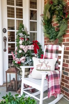 a white rocking chair sitting on top of a porch next to a christmas tree and wreath