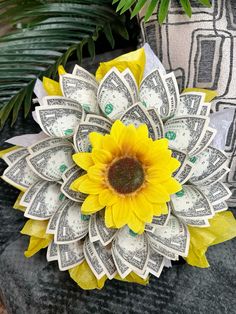 a sunflower made out of dollar bills sitting on top of a stone slab next to plants