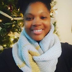 a woman wearing a scarf and smiling in front of a christmas tree