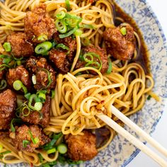 a blue and white bowl filled with noodles, meatballs and green onions next to chopsticks