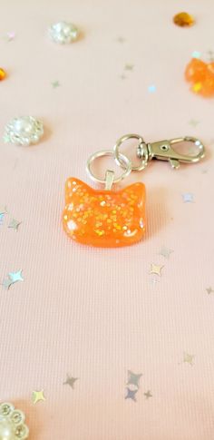 an orange cat shaped keychain sitting on top of a pink table covered in confetti