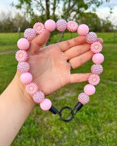 a hand holding a pink beaded bracelet in the shape of a heart with flowers on it