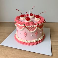 a pink and white cake with cherries on it sitting on top of a table