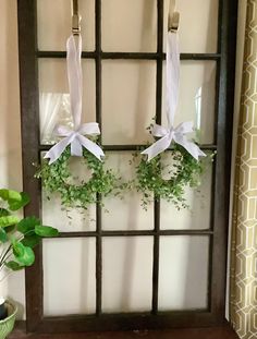 two wreaths with white bows hang on a window