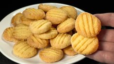 a hand holding a white plate filled with small round cookies on top of a black table