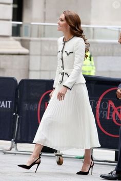 a woman in a white dress and black shoes is walking down the street with her hand on her hip