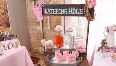 a table topped with lots of cakes and desserts next to a sign that says watering hole