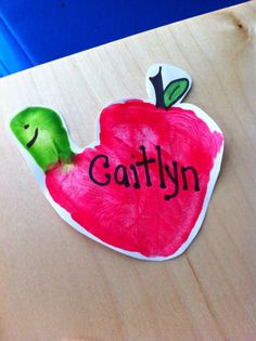 a wooden table topped with an apple shaped paper cut out of the shape of a worm