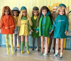 six dolls are lined up in front of a wall with yellow and green stripes on it