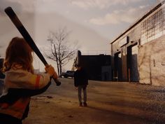 a woman holding a baseball bat while standing next to a man on the side walk