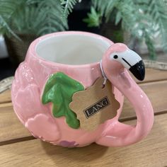 a pink ceramic flamingo mug with a tag on it's handle sitting on a wooden table