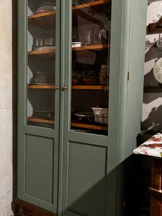 a green china cabinet with glass doors and shelves