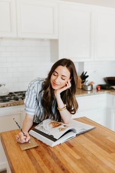 a woman sitting at a kitchen table writing on a book