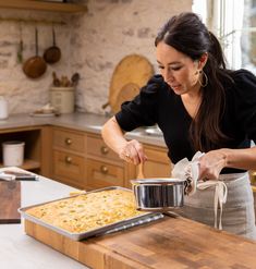 a woman preparing food in a kitchen on top of a wooden counter next to a pan