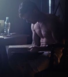 a shirtless man sitting at a table in the dark