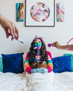 a woman sitting on top of a bed with a cat in her lap and another person holding a toothbrush